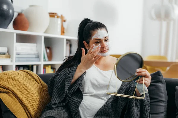 Woman is looking in the mirror and applying a face mask