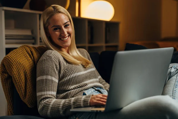 A happy Caucasian woman works on laptop and looks at the camera