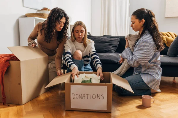 Three friends putting clothes in a box for donation