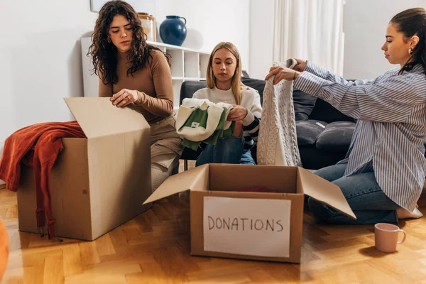 Three woman are packing clothes in boxes for donation