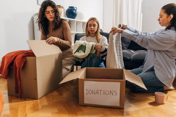 Три женщины упаковывают одежду в коробки для пожертвований
