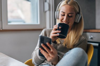 Blond woman uses her phone and drinks coffee