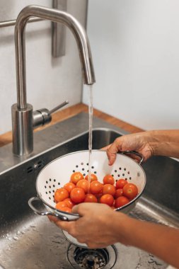 Cherry tomatoes are being washed in the strainer