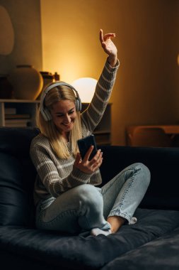 Beautiful young woman with headphones is looking at the phone and smiling