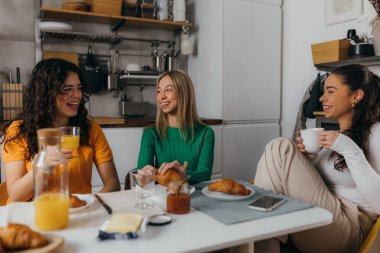 Three beautiful friends sit in the kitchen and talk
