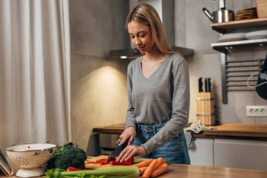 Blond woman is chopping red pepper in the kitchen