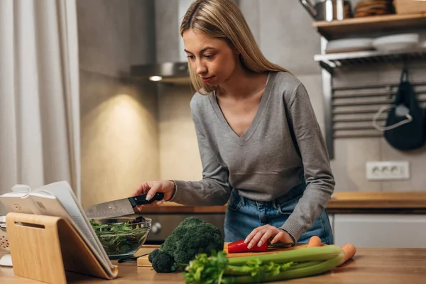 stock image A blonde woman checks a recipe book for ingredients