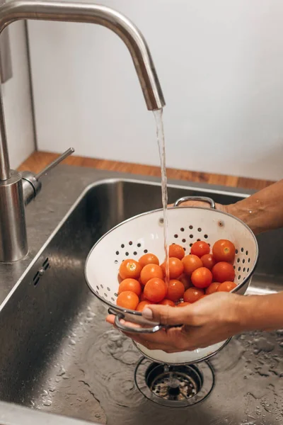 Cherry tomatoes are being washed in the strainer