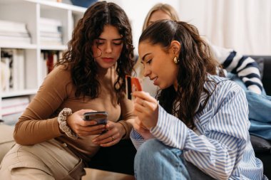 Kız arkadaşlar internetten cep telefonuyla alışveriş yapıyorlar.