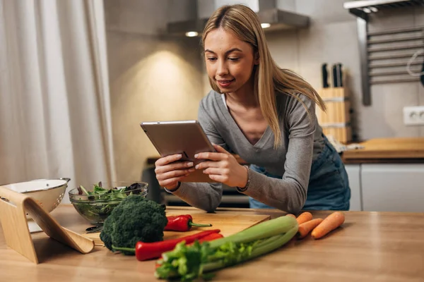 stock image A woman leans on the table and looks at a recipe on tablet