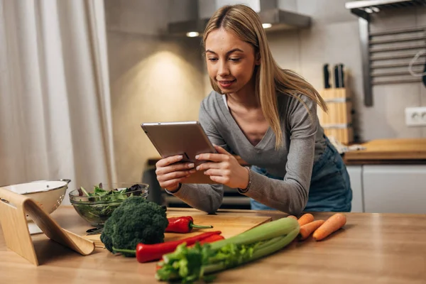 Stock image A woman leans on the table and looks at a recipe on tablet