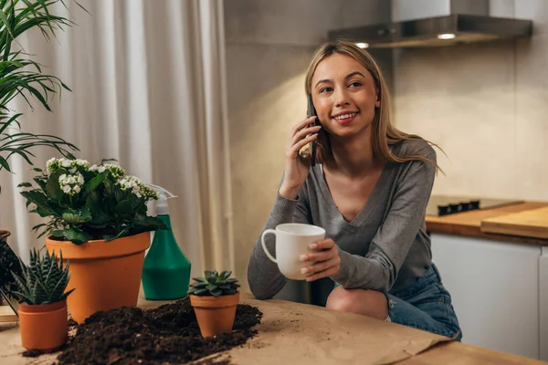 stock image A pretty blond woman is enjoying a phone call after planting her houseplants