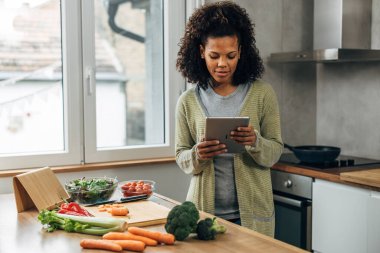 Bir kadın mutfakta duruyor ve tabletten vegan tarifi okuyor.