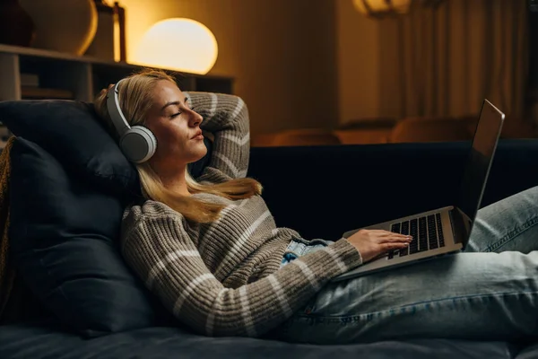 stock image A blond woman with headphones falls asleep with laptop on her lap