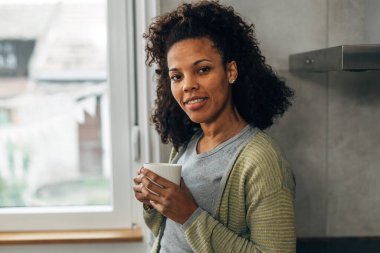 Karışık ırktan bir kadın elinde fincanla kameraya bakıyor.