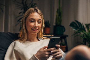 Genç bir kadın cep telefonu kullanıyor ve kameraya bakıyor.