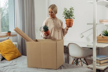 Genç bir kadın kutudan bitkileri topluyor.