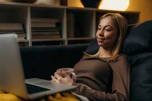 一个金发女人坐在沙发上 看着笔记本电脑 — 图库照片