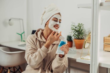 Bir kadın yüz maskesi takarken aynaya bakıyor..