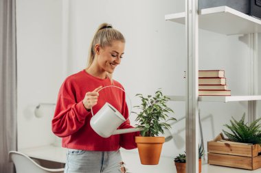 Genç ve güzel bir kadın çiçekleri suluyor.