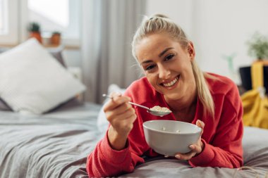 Güzel genç bir kadın yatakta yulaf ezmesi yiyor.