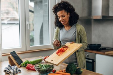 Karışık ırk kadını salataya doğranmış kırmızı biber ekliyor.