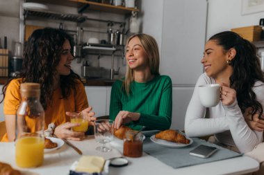 Üç kadın mutfakta oturmuş konuşuyor.