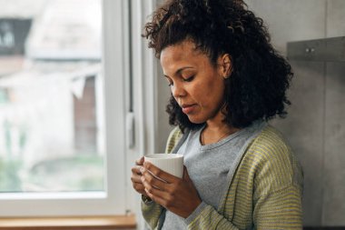Düşünceli bir kadın elinde bir bardak tutuyor.
