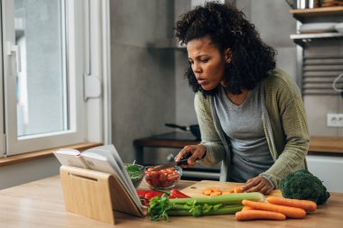 Karışık ırktan bir kadın yemek tarifi kitabı kullanıyor.