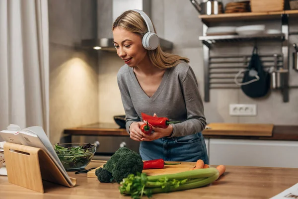 stock image Happy young woman is listening to music and cooking