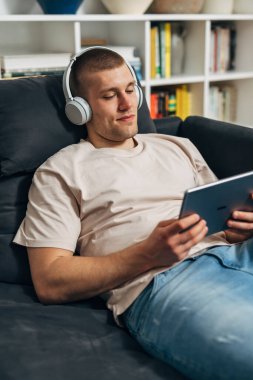 Bir adam kanepede yatıyor ve tablet bir cihaz kullanıyor.