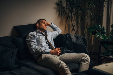 Yorgun bir işadamı kanepede oturuyor ve düşünüyor.