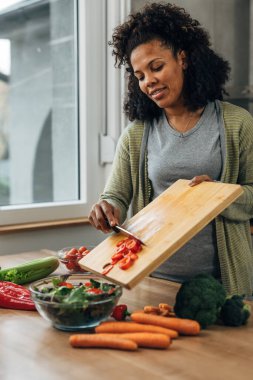 Gülümseyen melez bir kadın mutfakta sebze salatası yapıyor.