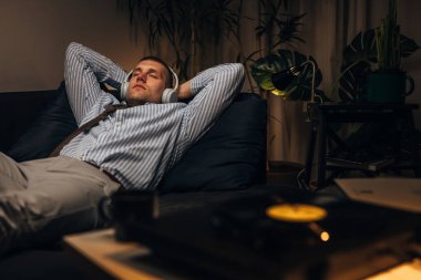 Kulaklıklı bir işadamı kanepeye uzanıp plakları dinlemekten zevk alır.