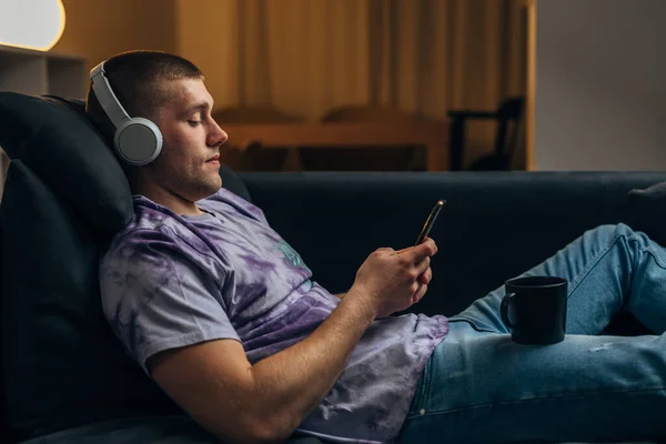 一个年轻的白人男子舒适地坐在沙发上 用智能手机 — 图库照片