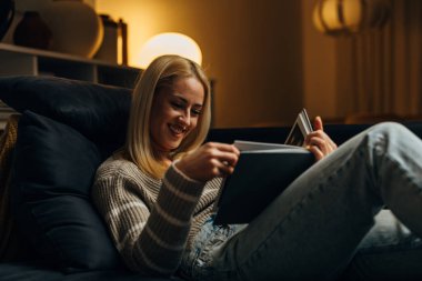 Güzel sarışın bir kadın evde kitap okuyor.