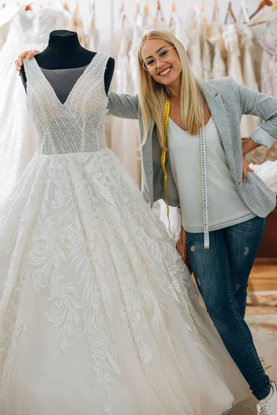 Woman works in a wedding dress salon and stands next to a dress on a model