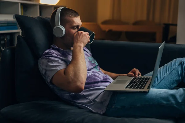 ソファに座ってコーヒーを飲んでノートパソコンを使ってる白人男性のプロフィール — ストック写真