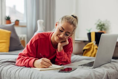 Bir kız üniversite öğrencisi yatağında online ders alırken çok fazla alır.