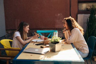 Anne-kız kaynaşıyor. Arka bahçede kahvaltı ederken kahkahalar atıyor..