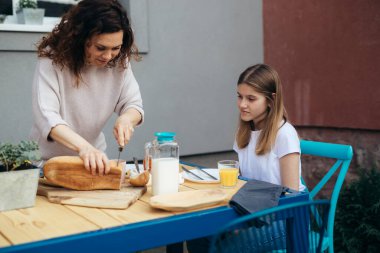 Annem kızıyla birlikte bahçede kahvaltı için ekmek kesiyor.