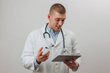Kafkasyalı bir doktor tablete bakıyor ve bir hastayla görüntülü konuşuyor..