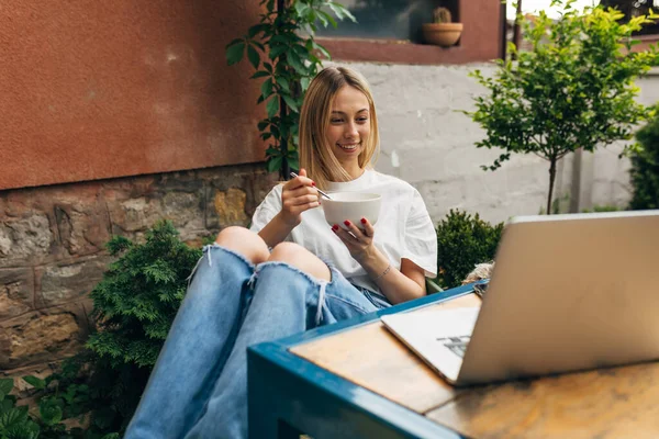 stock image A beautiful young blond woman sits in the backyard and looks at laptop