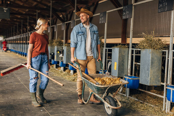A woman and a man work at the animal farm and walk in a barn.