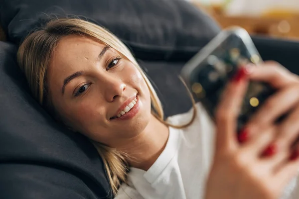 一个年轻女人躺在床上用她的手机拍照 — 图库照片