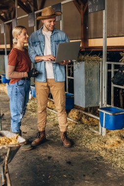 İki genç insan bir hayvan çiftliğinde dizüstü bilgisayarla inceleme yapıyorlar..
