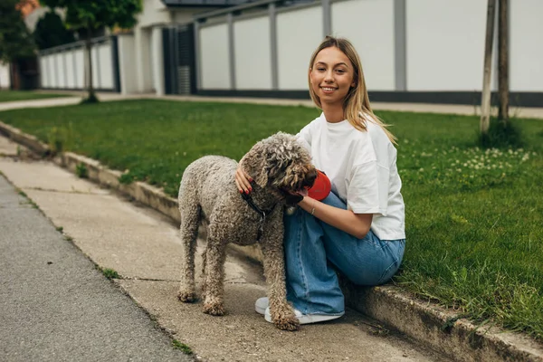 美しい若い女性が道の脇に座って犬を抱きしめる — ストック写真