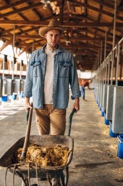 Çiftçi elinde samanla büyük bir ahırda yürüyor..