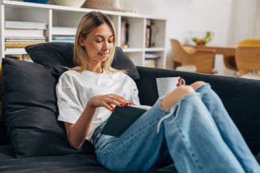 Bir kadın kanepede oturuyor ve güzel bir kitabın tadını çıkarıyor..