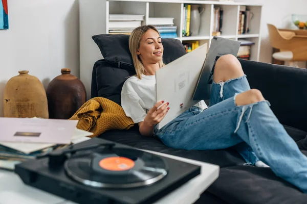 stock image A pretty woman listening to music on gramophone and looking at t the covers of her records.